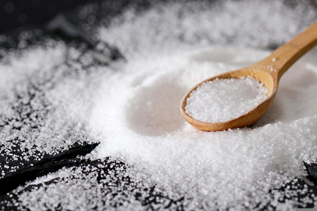 wooden small spoon filled with salt, black background with spilled salt