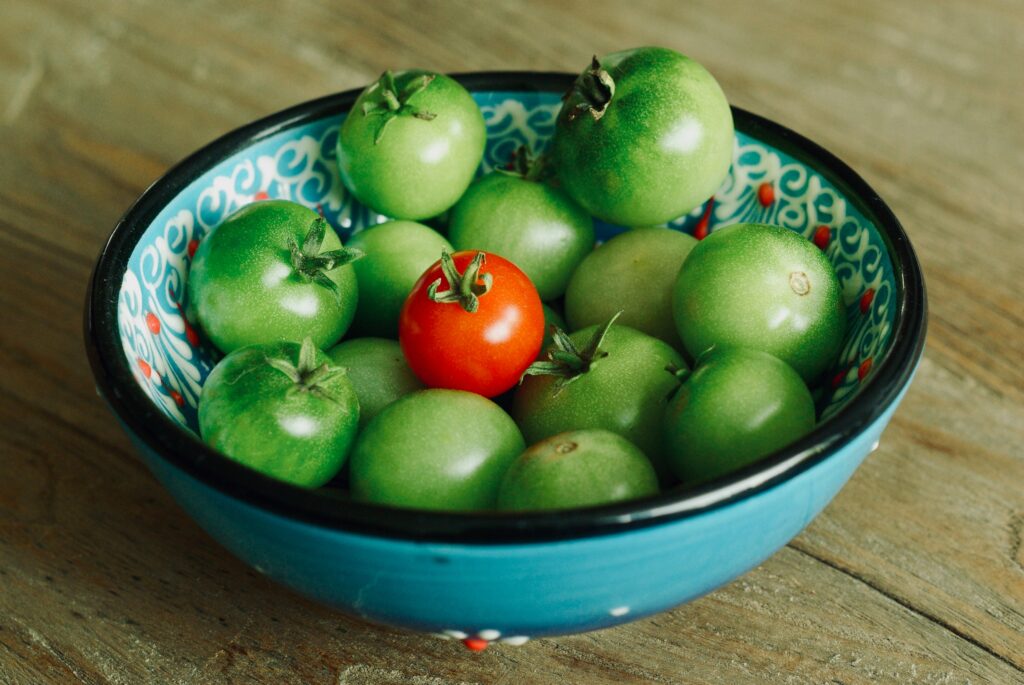 one red tomato in a bowl full of green tomatoes on the table